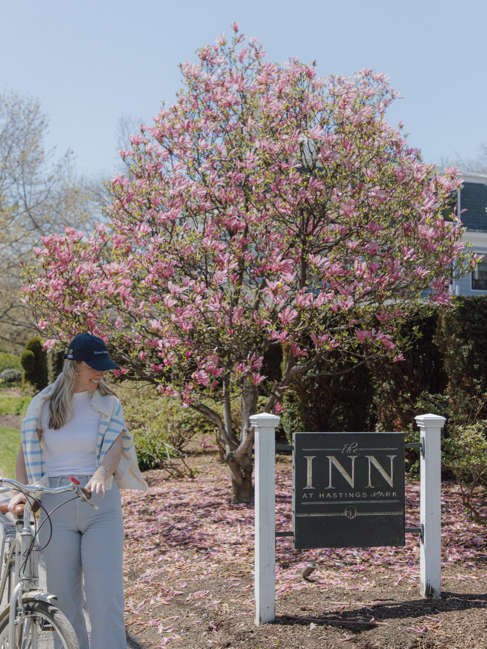 woman in a bicycle by the inn sign with a cherry blossom tree in the background