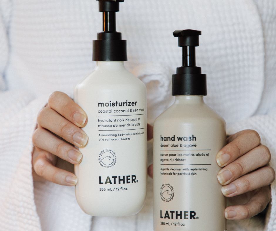 Person in a white robe holding two LATHER brand bottles: moisturizer (coastal coconut) and hand wash (desert aloe & agave).