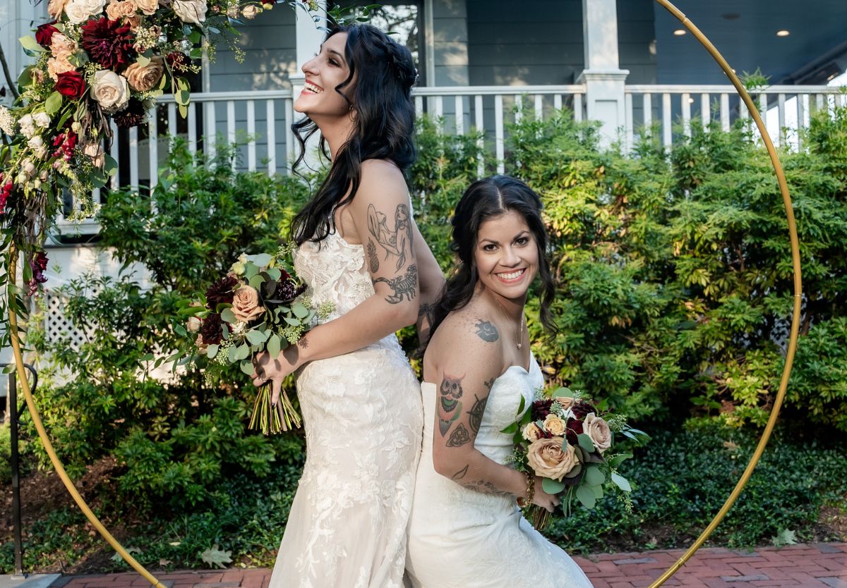 Brides posing together outsides in a floral arch